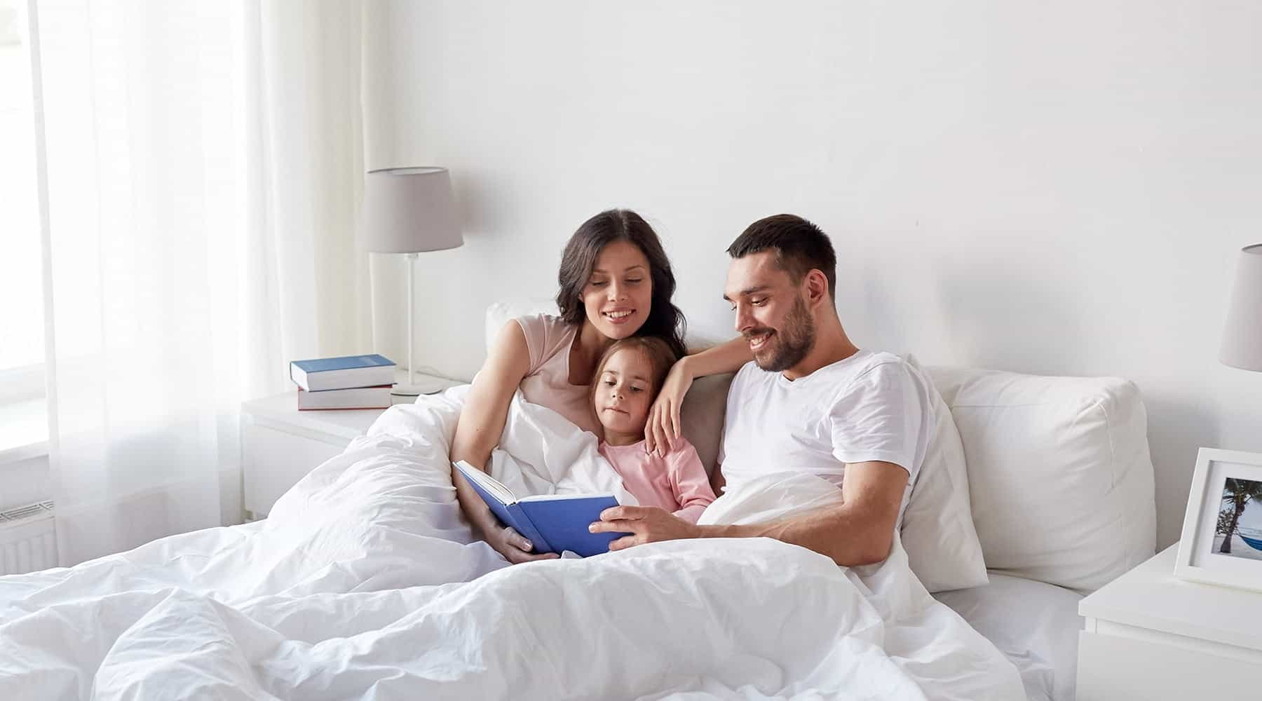 Una familia, padre, madre e hija, leyendo un libro sobre la cama de un cuarto